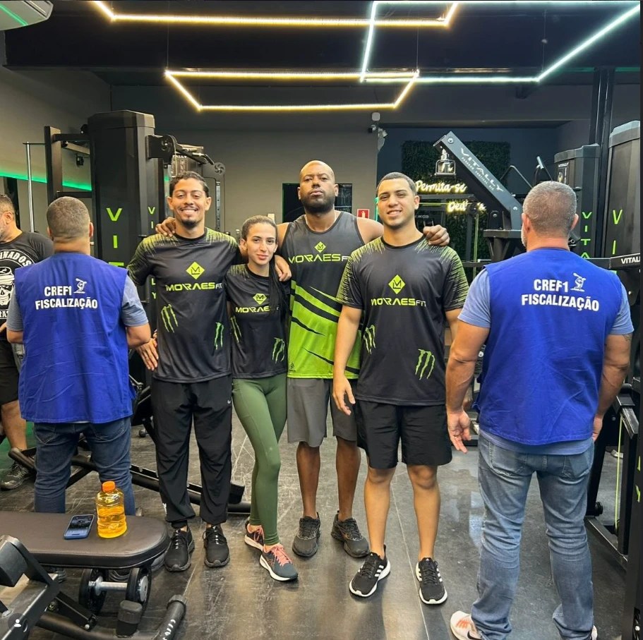 Professores da Moraes Fit com a camisa da academia, entre os dois fiscais do CREF1 de colete azul, na sala de musculação
