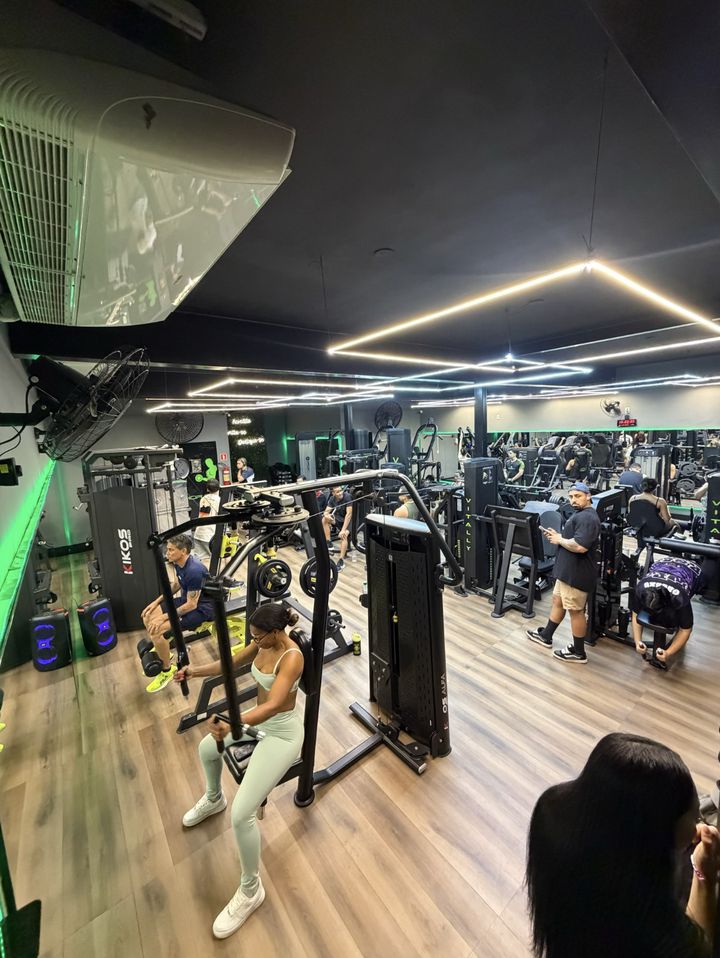 Ar-condicionado e ventiladores sobre a sala de musculação, com aluna treinando no voador